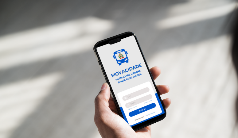 Uma mão segurando um celular, a tela mostra a página de login do app Movacidade