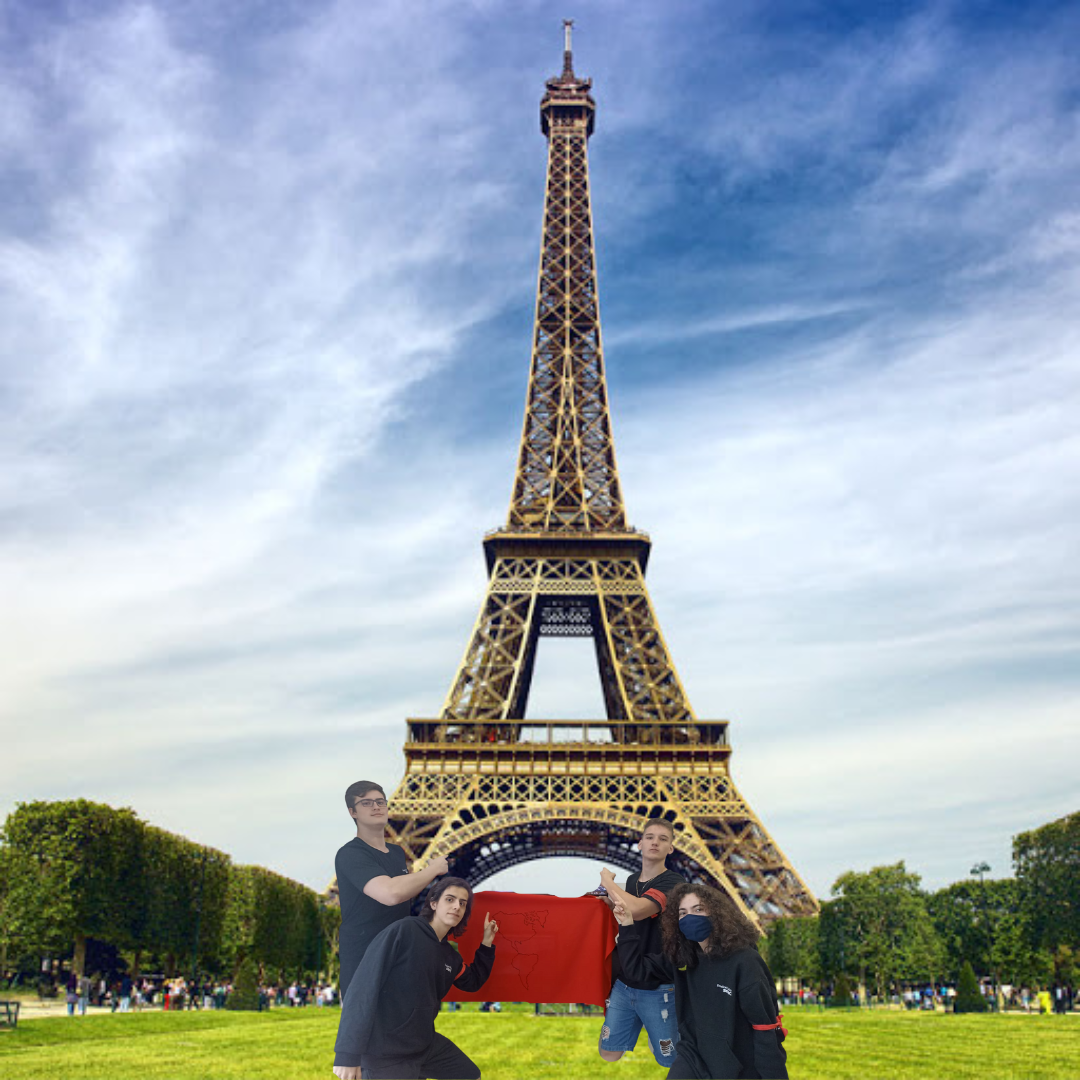 4 integrantes da equipe apontando para a Torre Eiffel, e segurando a bandeira da equipe vermelha.